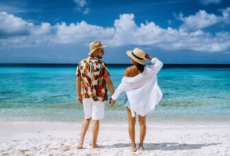 Couple holding hand while on a sandy beach looking at the water