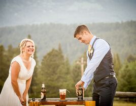 A bride and groom pouring a black and tan drink into a beer glass at their outdoor unity ceremony.