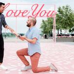 Couple getting engaged in front of pink I Love You sign