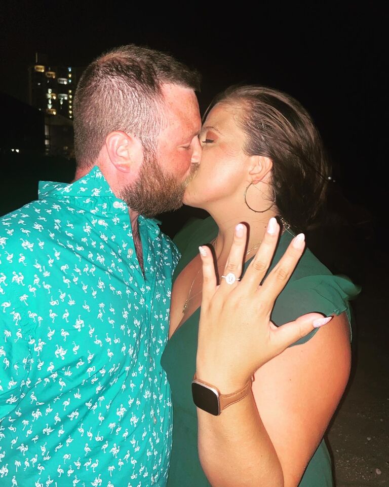 On a shared family trip to Myrtle Beach, Sean proposed to Amanda with a beautiful scene of the words "Marry Me" written in lights surrounded by candles and rose petals. They were engaged!!