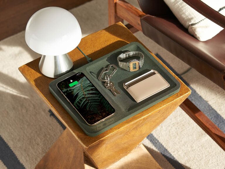 Green valet tray on nightstand with smartphone charging wirelessly, watch, wallet and keys 
