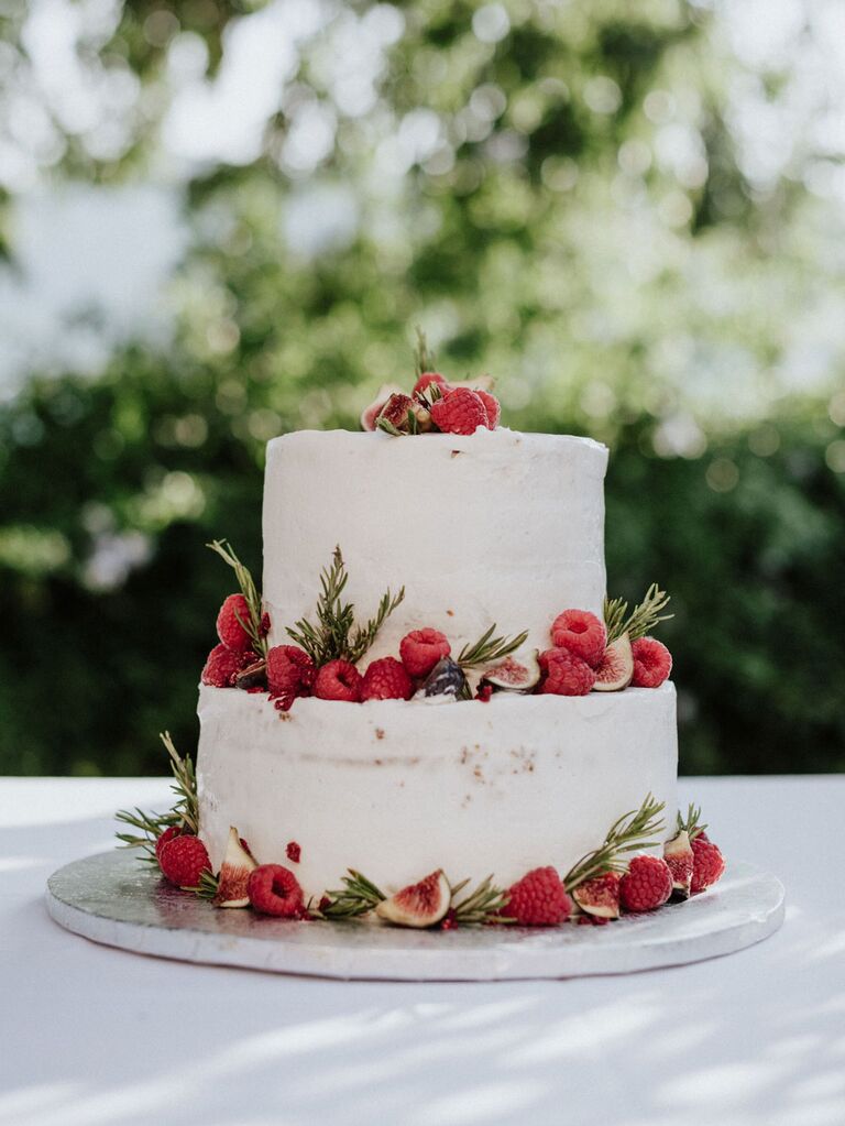 Two-tier rustic cake with white icing covering with fresh berries and greenery