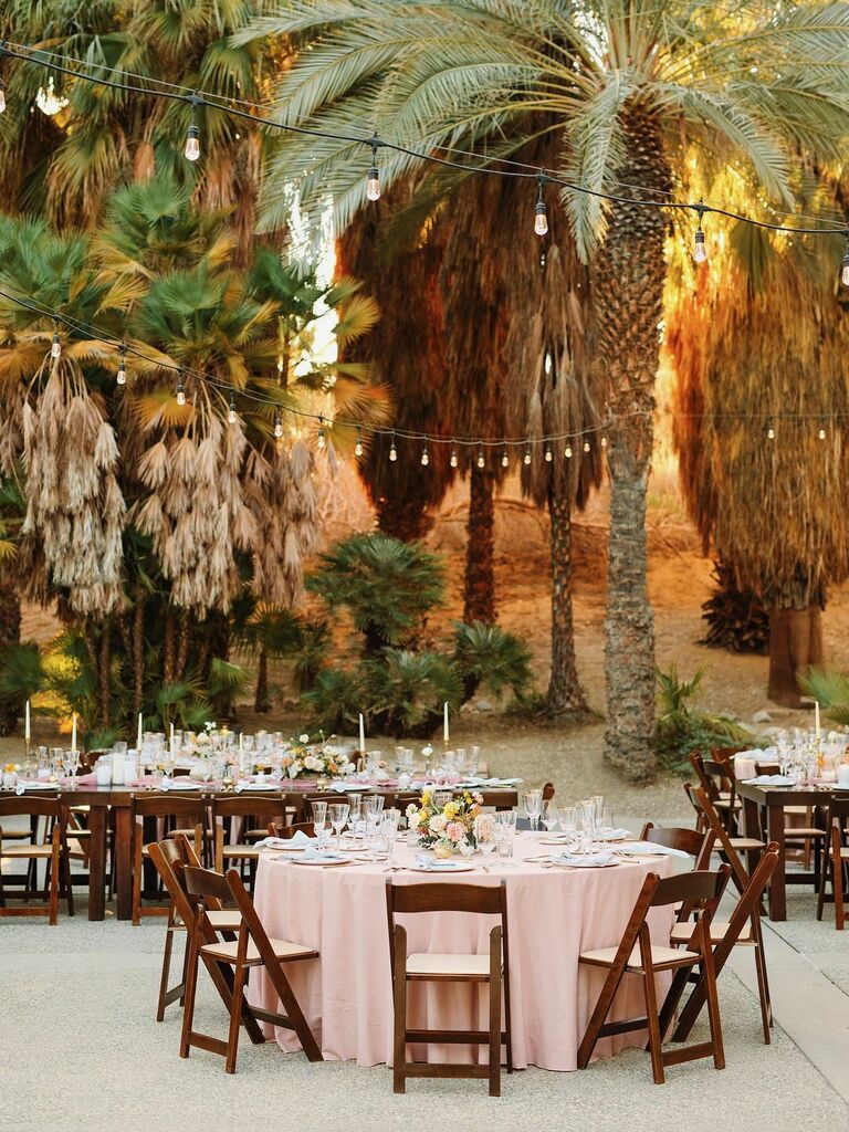 round banquet table with blush table cloth and dark wood folding chairs surrounded by palm trees