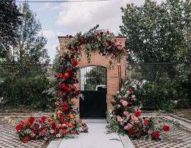 dramatic red and pink ombre floral arch at outdoor wedding ceremony