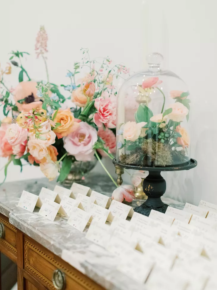 escort card table decorated with cloche-covered floral arrangement
