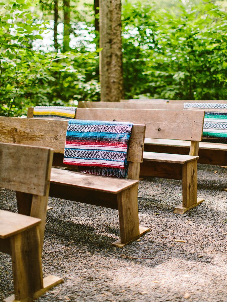 wooden benches at outdoor wedding ceremony with colorful woven blankets on the end