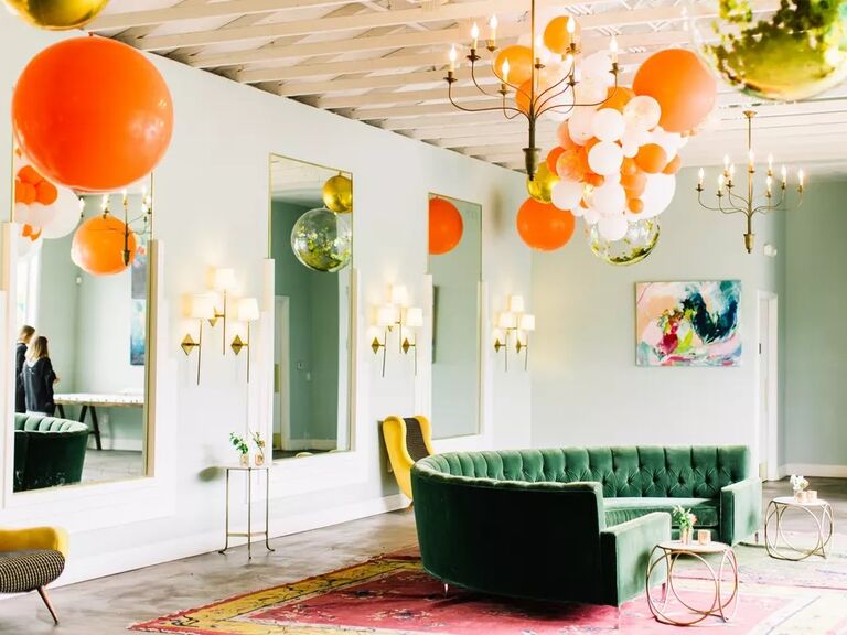 Chic event space with high ceilings, gold accents, and orange balloons. 