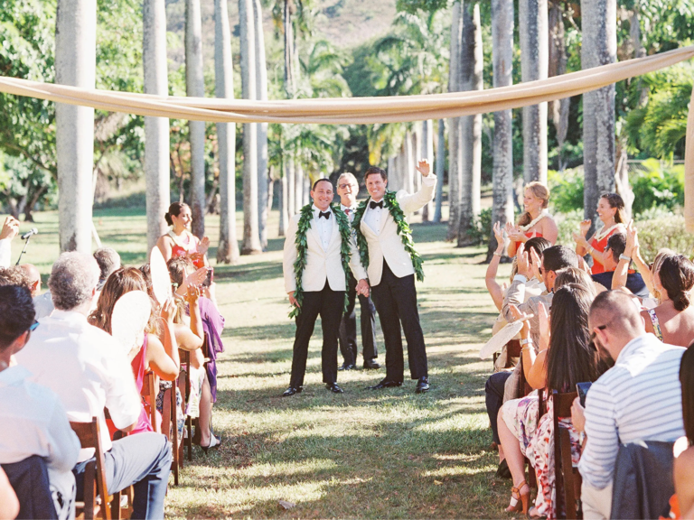 Grooms smiling with officiant at outdoor wedding ceremony in Hawaii