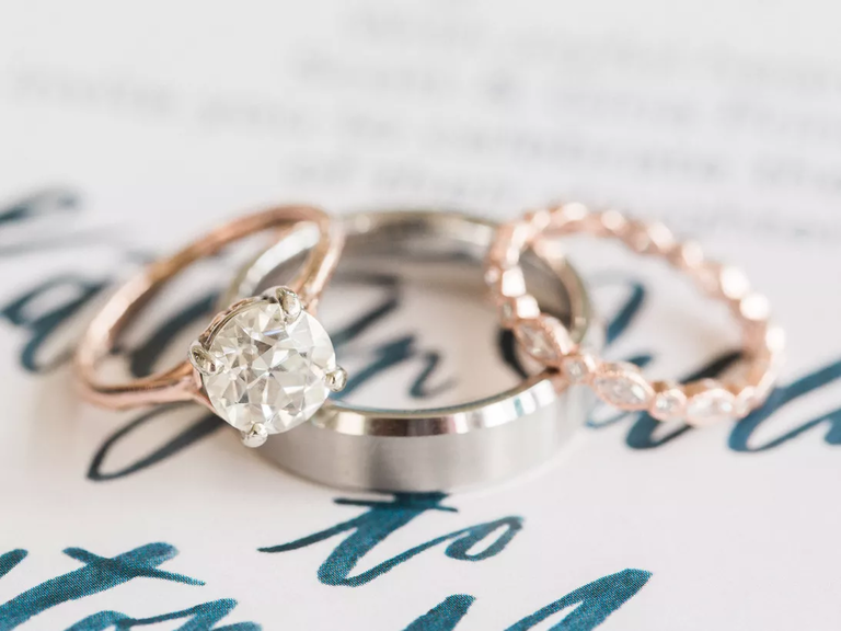Two rose gold engagement rings sit atop a silver wedding band.