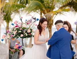 Couple exchanging rings at beachfront ceremony with colorful bouquets