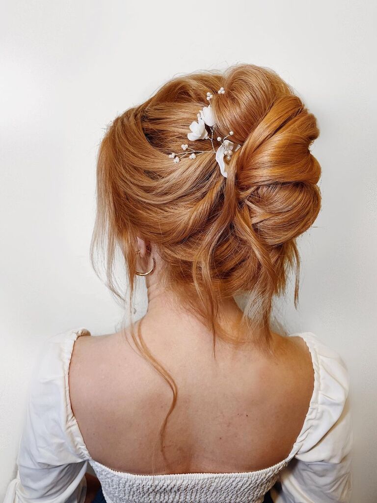 Messy high bun wedding updo for long hair with floral accessory