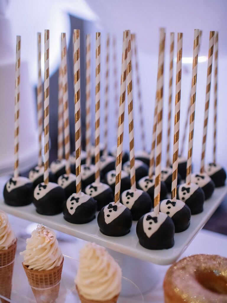 wedding cake pops designed to look like miniature black tuxedos served with gold striped sticks