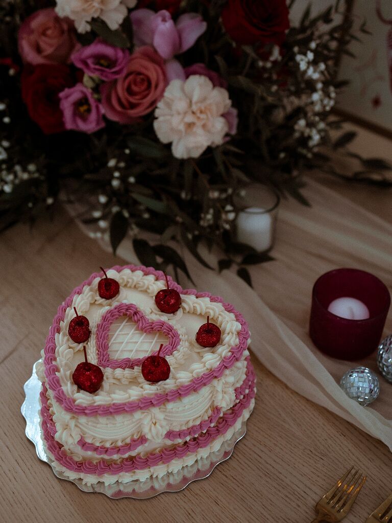heart shaped wedding cake with pink and white piping and red glitter cherries