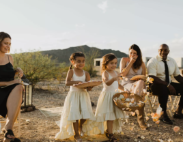 Toddler flower girls in white dresses walking down aisle at outdoor wedding