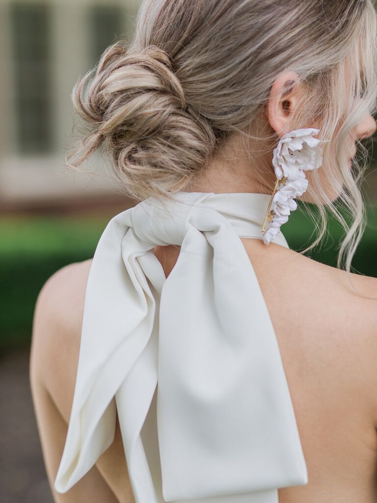 Bride from behind wearing statement earrings and bow-tie top with hair in bun