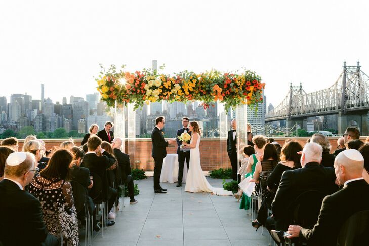 Couple standing in front of chuppah with acrylic legs in front of New York skyline.