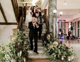 A wedding band leads the happy couple down the stairs of their venue.