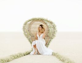 Cool edgy bride wearing Hayley Paige wedding dress sitting on rattan peacock chair at Black Rock desert Nevada