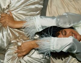 Woman laying fown on a bed grabbing a pillow behind her head