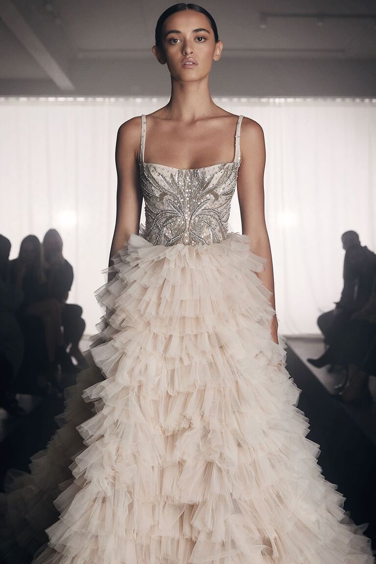 Model wears a beautiful wedding gown with a ruffle-tiered skirt and an embellished bodice. 
