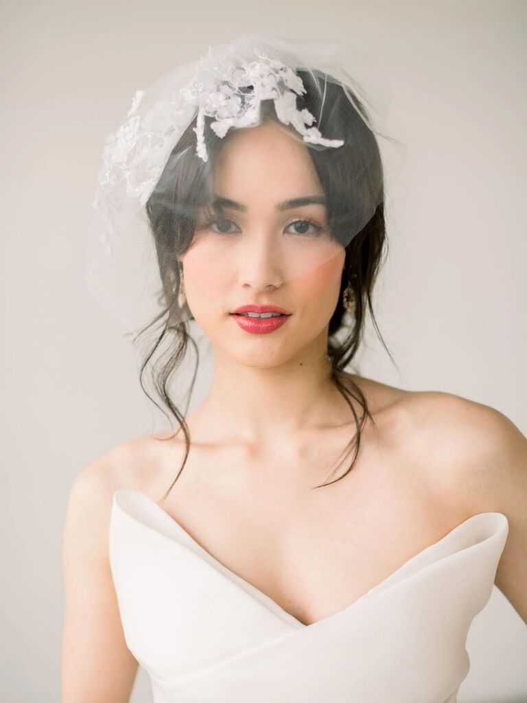 Model wears a birdcage veil with floral embroidery. 