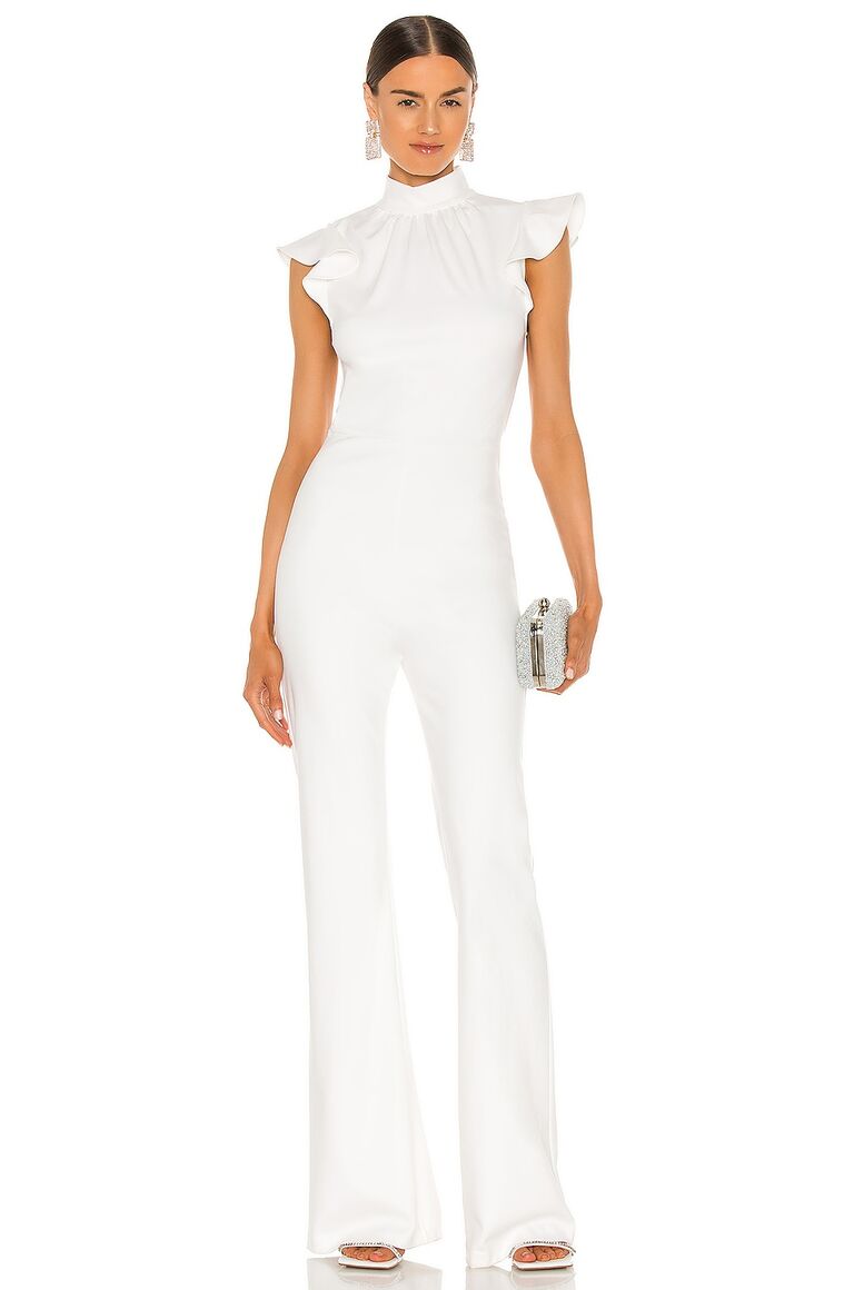 Model wears a white jumpsuit with a high neckline and ruffled short sleeves. 