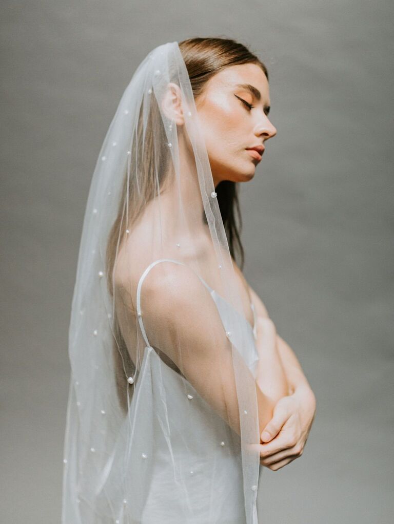 Model wears a long sheer veil embellished with pearls. 