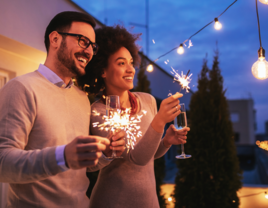 Couple holding champagne flutes and sparklers at rooftop engagement party