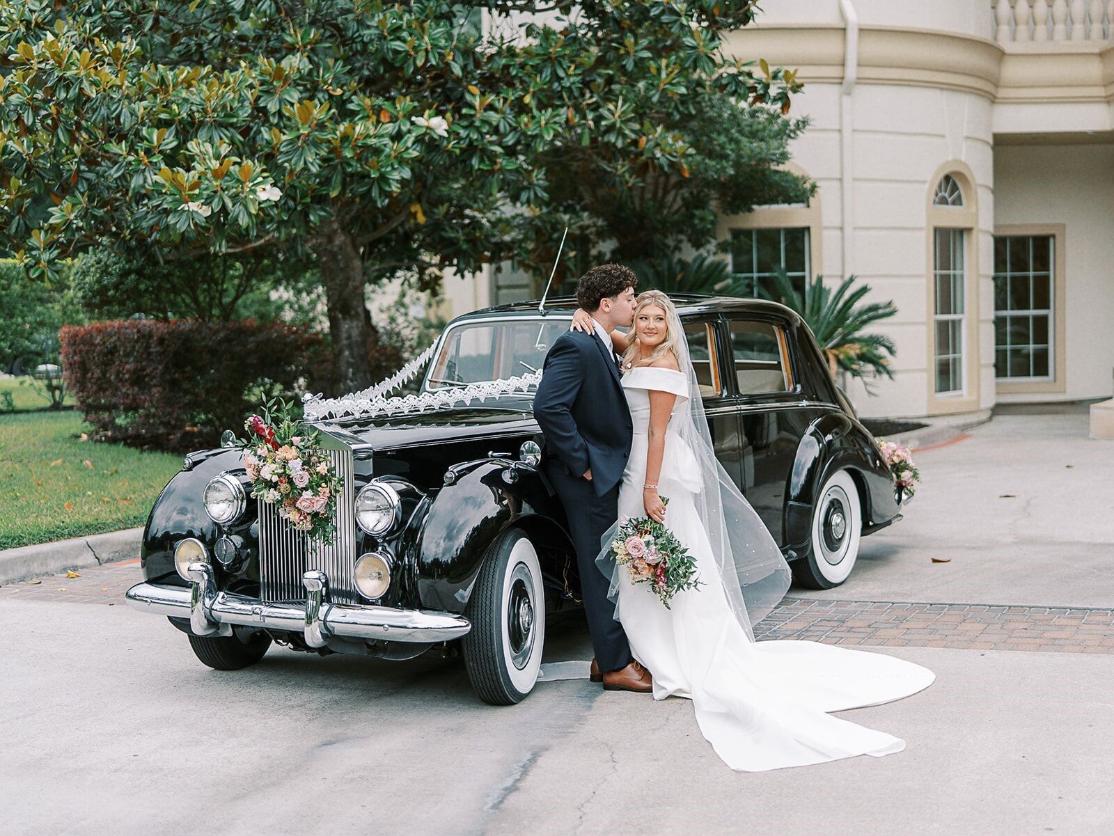 Couple posing in front of a black vintage wedding car