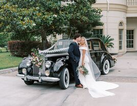 Couple posing in front of a black vintage wedding car