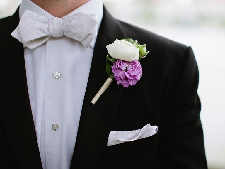 A boutonniere with a purple camellia flower on a tuxedo lapel