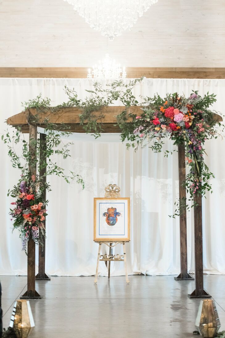 Rustic wood chuppah covered with greenery in front of wall draped with white fabric.