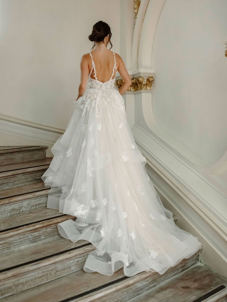 Model walks up steps wearing a long flowing wedding gown. 