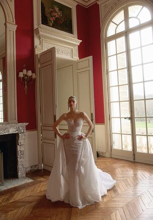 Taffeta, lace, and tulle unite in Nymphea, a transformable design from the WONA Concept Maison Blanche collection. The fitted silhouette features a strapless neckline, a sculpted corset bodice, and fine beading with pearls that catch the light. A low, open back balances the front profile before flowing into a court train. For an alternate presentation, a detachable overskirt layer from matching textiles shifts the profile into a fuller A-line look with a sweeping chapel-length train. This design balances texture with structured lines for a bride seeking both tailored precision and romantic movement.
