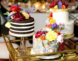 trio of colorful wedding cakes on a gold bar cart decorated with red, yellow, purple and orange flowers