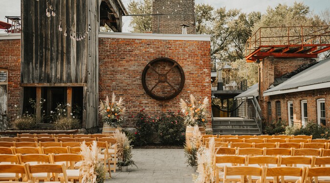 Rustic outdoor wedding ceremony venue with wooden chairs, floral aisle decor, and industrial brick backdrop at City Winery