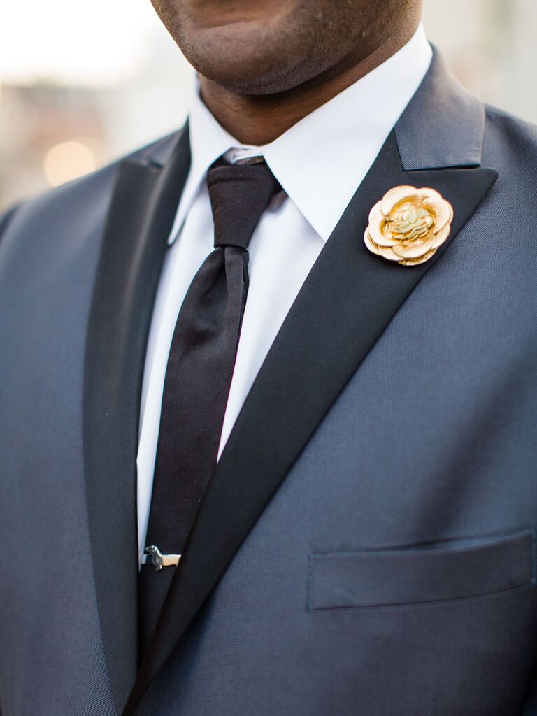 groom wearing navy blue tuxedo with gold flower brooch on lapel