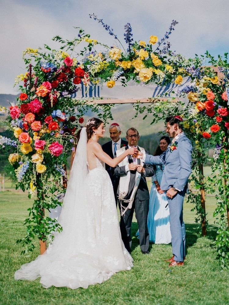 couple underneath colorful floral chuppah at Jewish wedding