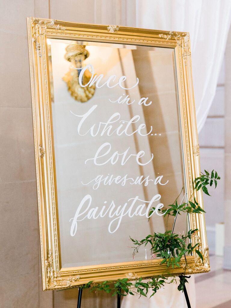 mirror wedding sign in gold frame and quote written in white calligraphy: 