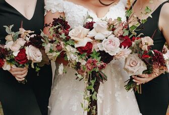 close up of bride and bridesmaids holding winter wedding bouquet with light pink garden roses, dark red roses and ivy vines