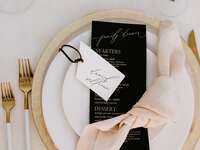 winter wedding place setting with gold charger plates and flatware, black menu card and blush linen napkin
