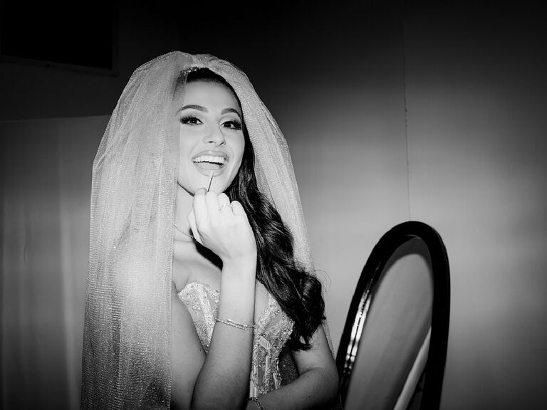 Black and white photo of bride applying lip gloss in veil