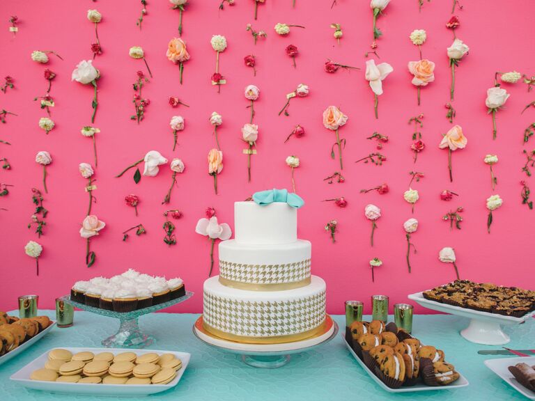 Individual flower stems taped on pink wall around wedding cake and dessert spread