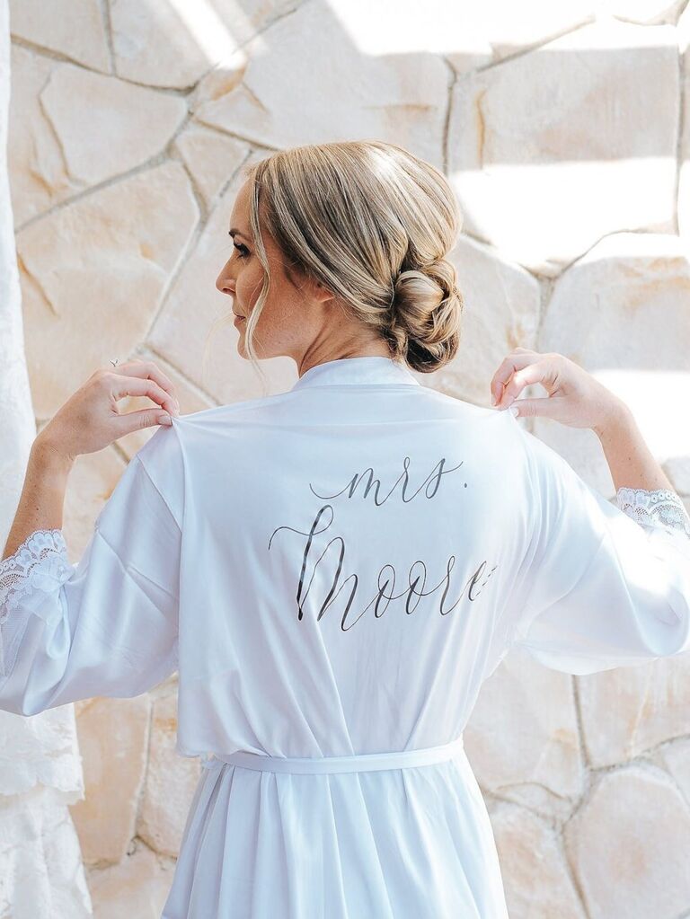 Model wearing white robe with lace details and their name neatly printed on the back