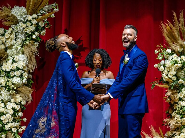 grooms in blue suits laughing during wedding ceremony