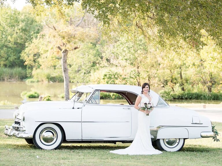 Bride standing beside a vintage white wedding car