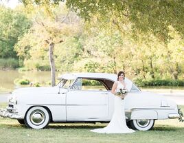 Bride standing beside a vintage white wedding car