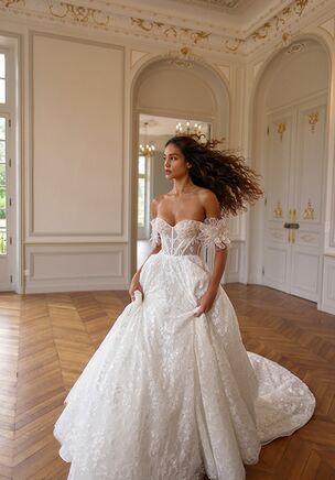 Delicate A-line dress with a cold-shoulder neckline and voluminous floral appliqués over the draped sleeves. The corset is decorated with flowers and beads, embellishing the bra and cascading down the gown in a shiny floral pattern. The veil echoes the design with appliqués at the hem.