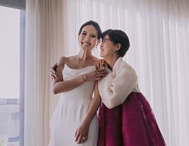 bride in wedding dress smiles with mother of the bride wearing a korean hanbok