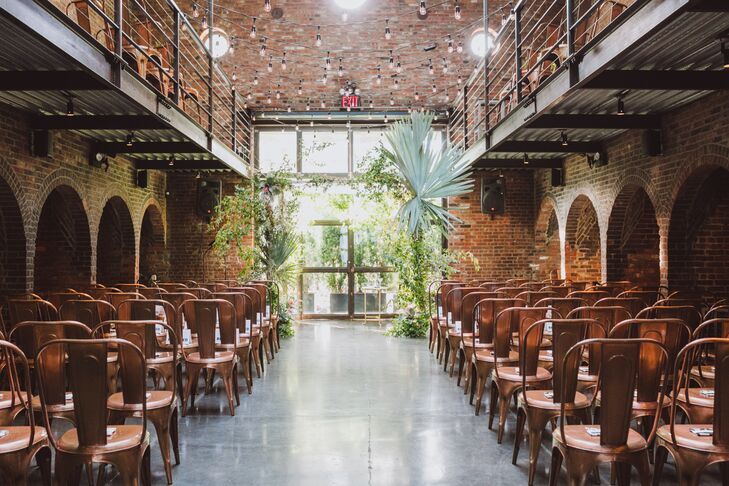 Palm-covered chuppah in industrial loft venue surrounded by copper tolix chairs.